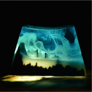 May include: A clear resin sculpture with a blue and white swirling design. The resin is shaped like a mountain range with a white base.