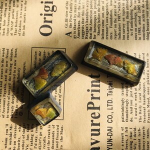 May include: Four small rectangular resin keychains with pressed dried leaves and flowers inside. The keychains are in shades of brown, green, and yellow. The text "avure Print YUN-DAI CO., LTD. Taipei" is printed on a white background.