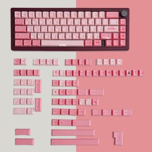 Op de afbeelding: Een set roze en witte toetsen voor een 60% toetsenbord. De toetsen hebben verschillende ontwerpen, waaronder sterren, harten en andere symbolen. De toetsen zijn gerangschikt in rijen en kolommen, waarbij de bovenste rij is gelabeld met de functietoetsen (F1-F12). De onderste rij bevat de modificatietoetsen (Ctrl, Alt, Shift en Win). De toetsen zijn gemaakt van duurzaam plastic en zijn ontworpen om te passen op standaard mechanische toetsenborden.