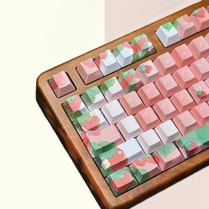 May include: A wooden keyboard with pink and white keys featuring a strawberry and leaf design. The keys are labeled with Japanese characters.