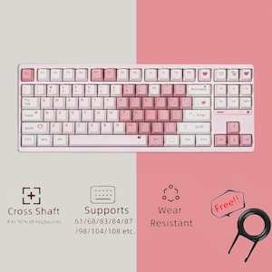 Puede incluir: Un teclado rosa y blanco con una tecla en forma de corazón. El teclado tiene un diseño de eje cruzado y admite diseños de teclado de 61, 68, 83, 84, 87, 98, 104 y 108 teclas. El teclado es resistente al desgaste y viene con un extractor de teclas.