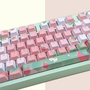 May include: A light green keyboard with pink keys and a strawberry and floral design. The keys are labeled with letters, numbers, and symbols. The keyboard has a space bar with a green and white floral design.