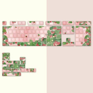May include: A set of pink and white keyboard keycaps with a strawberry and leaf design. The keycaps are arranged in a keyboard layout with the function keys, number keys, and letter keys visible.