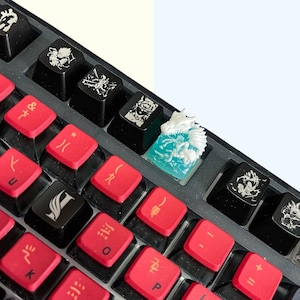 Puede incluir: Un teclado negro con teclas rojas y una tecla impresa en 3D de color blanco y azul con un diseño de dragón.