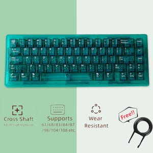 Könnte beinhalten: Eine transparente, teal-farbene mechanische Tastatur mit transparenten Tastenkappen. Die Tastatur hat ein Standard-QWERTZ-Layout mit verschiedenen Funktionstasten. Das Bild zeigt auch einen Keycap-Abzieher und Symbole, die Funktionen wie Cross Shaft und Verschleißfestigkeit anzeigen.
