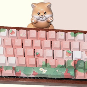 May include: A pink and white keyboard with a strawberry and floral design. The keyboard has a wooden frame and a small ceramic dog figurine on top.