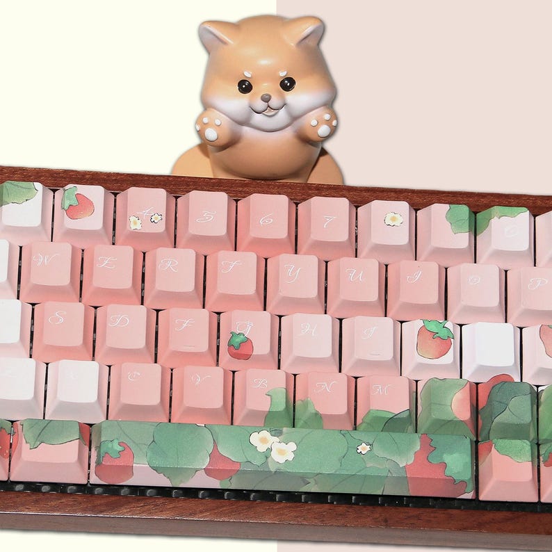 May include: A pink and white keyboard with a strawberry and floral design. The keyboard has a wooden frame and a small ceramic dog figurine on top.