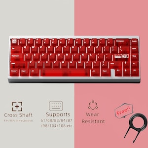 Puede incluir: Un teclado mecánico rojo y blanco con teclas rojas transparentes. El teclado tiene un marco blanco y una distribución QWERTY estándar. La imagen también muestra un extractor de teclas y texto que indica la compatibilidad del eje transversal y la resistencia al desgaste.