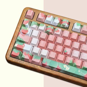 May include: A wooden keyboard with pink and white keycaps featuring a strawberry design. The keyboard has a light wood frame and a Japanese layout.