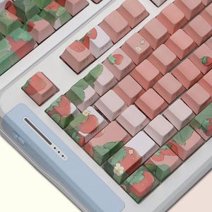 May include: A white keyboard with pink and green keycaps featuring a strawberry and leaf design. The keyboard has a light blue palm rest.