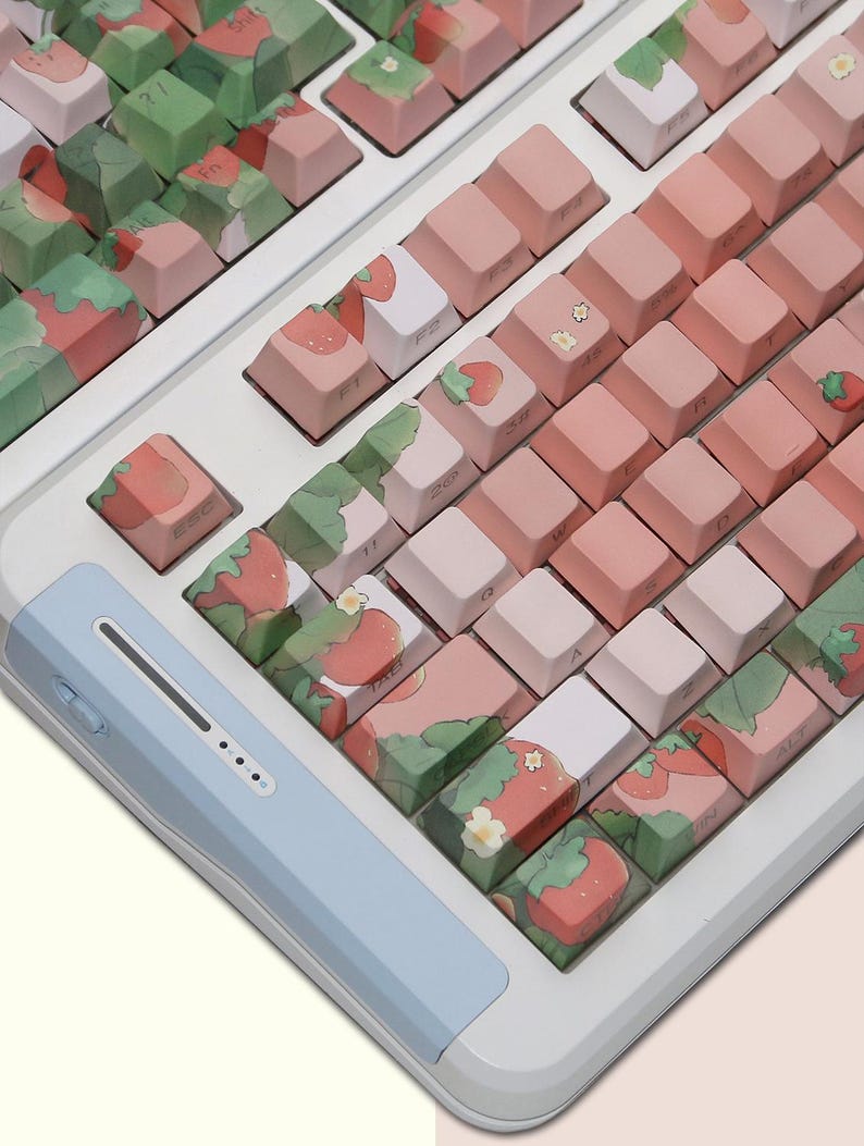 May include: A white keyboard with pink and green keycaps featuring a strawberry and leaf design. The keyboard has a light blue palm rest.