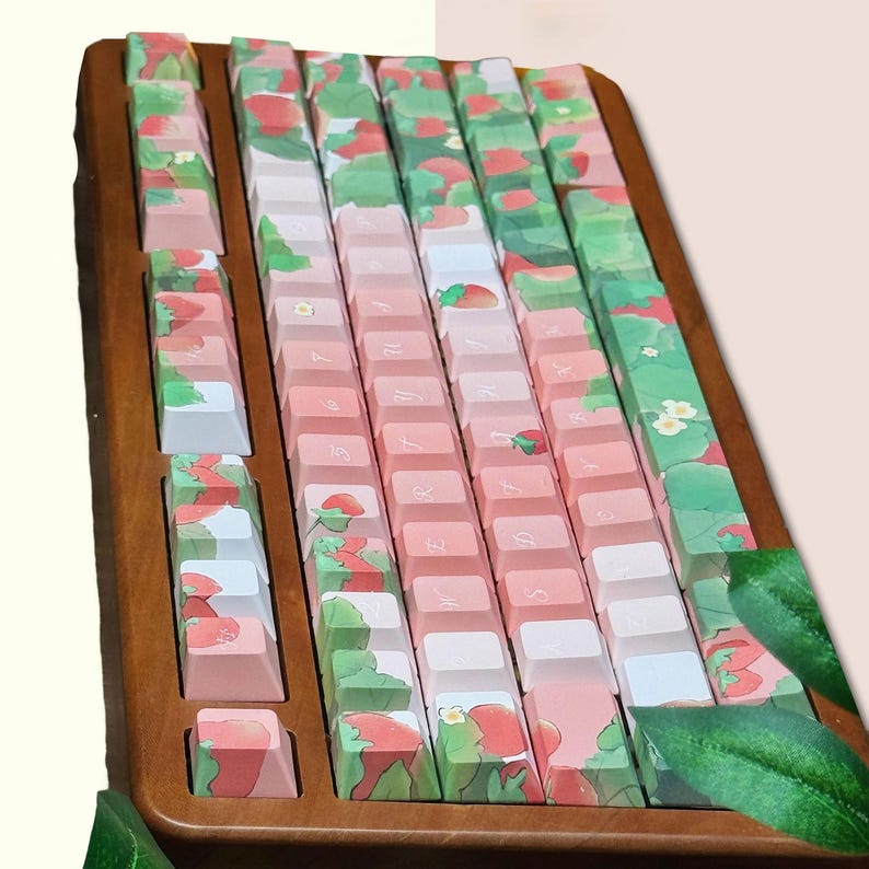 May include: A wooden keyboard with a strawberry and leaf design. The keys are pink and white with a light brown wooden frame.