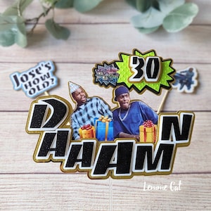 May include: A black and gold cake topper with the words "D'AAAM" and a picture of two men from the movie "Friday". The topper also includes a green and yellow star with the number "30" in black.
