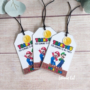 Può includere: Tre etichette di ringraziamento bianche con uno spago nero. Ogni etichetta presenta una moneta d'oro con un 1 sopra. Le etichette hanno un tema Mario e Luigi con il testo "Grazie per essere venuto alla mia festa".