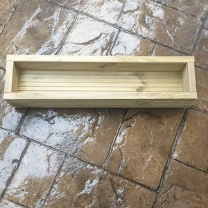May include: A wooden planter box with a rectangular shape and a natural wood finish. The planter is empty and ready for planting.
