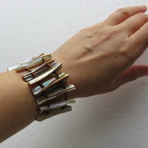 Op de afbeelding: Een armband gemaakt van iriserende schelpstukken en bruine kralen. De armband wordt om de pols gedragen.