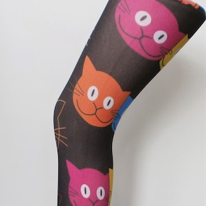 May include: Black tights with a colourful cat face pattern. The cat faces are in shades of pink, orange, blue and yellow.