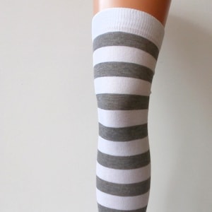 Könnte beinhalten: Oberschenkelhohe Socken mit horizontalen Streifen in Weiß und Grau. Die Socken werden auf einem Beinform präsentiert, um das Streifenmuster und die Länge der Socken zu zeigen.