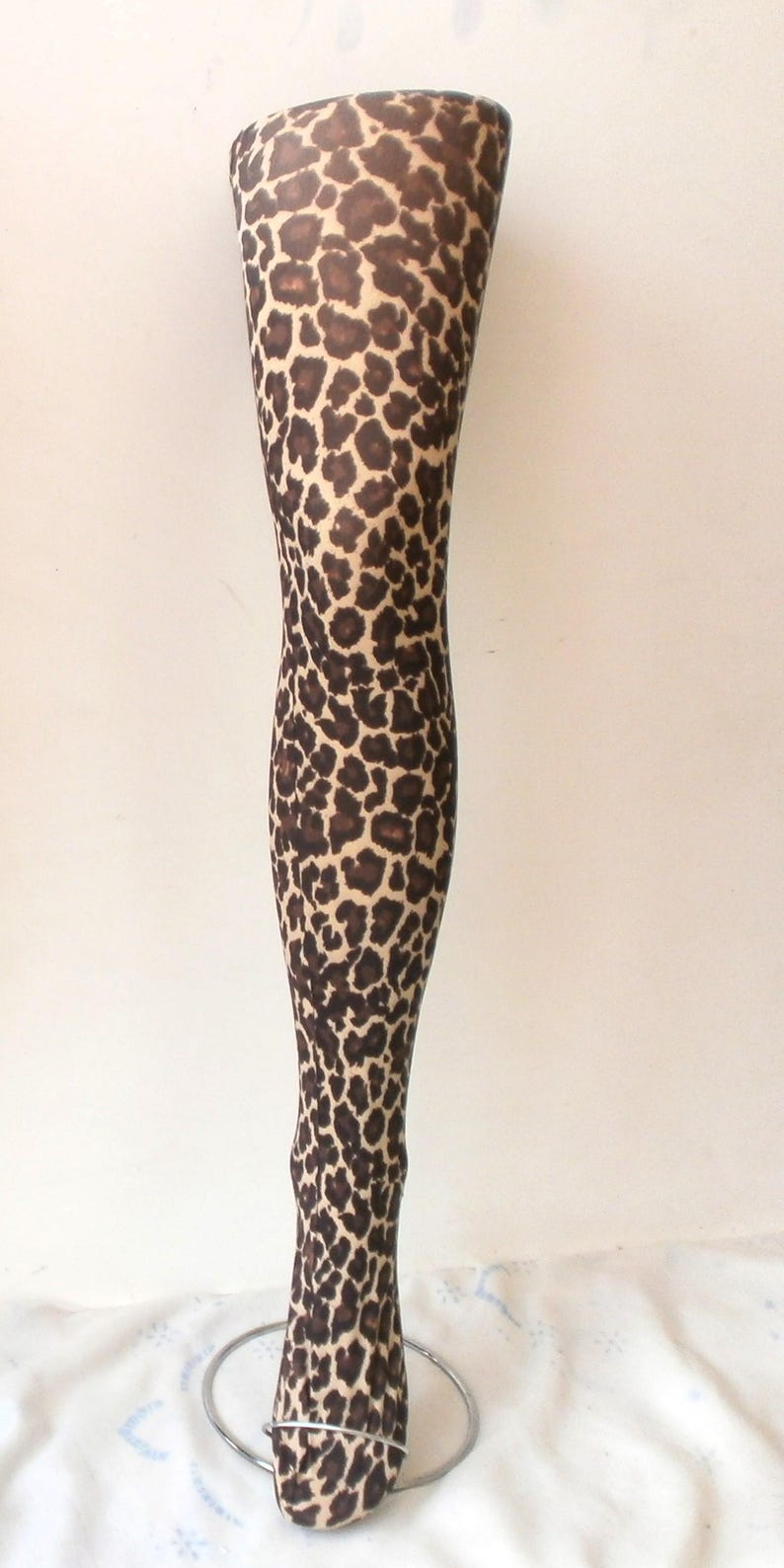 Puede incluir: Un maniqu&iacute; de pierna completa cubierto con un estampado de leopardo marr&oacute;n y beige. El maniqu&iacute; est&aacute; montado sobre una base circular de metal plateado, sobre un fondo blanco liso. Aproximadamente 100 cm de altura.