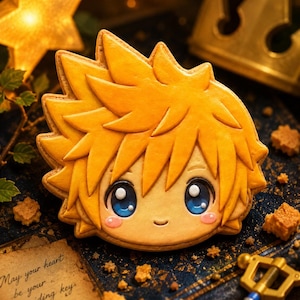 May include: A detailed, golden-yellow cookie shaped like a cartoon character's face with spiky hair and large blue eyes. The cookie is decorated with pink cheeks and sits on a dark blue surface with a golden star and crown in the background. The text "May your heart be your guiding key" is visible.