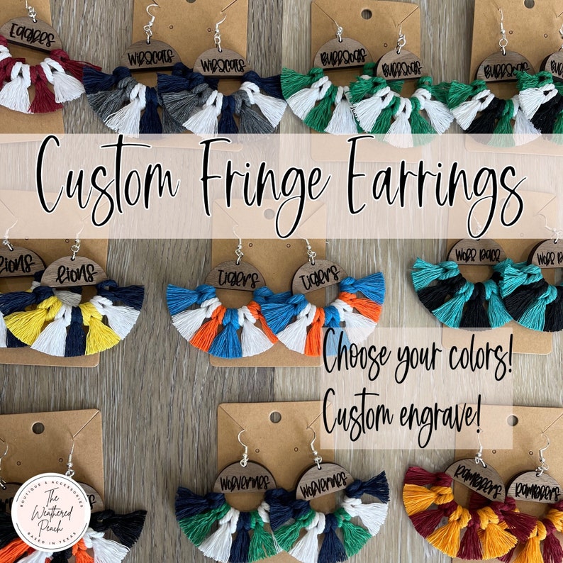 May include: Custom fringe earrings with various team logos and colors. The earrings are made of wood with a fringe of colorful yarn. The logos include Eagles, Wisconsin, Bulldogs, Lions, Tigers, Wolverines, and Rampage. The text on the earrings reads 'Choose your colors! Custom engrave!'.