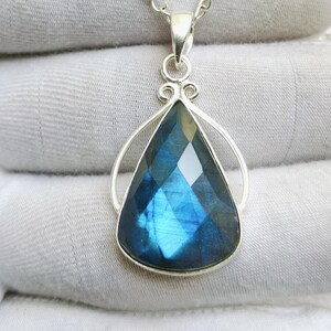 May include: A teardrop-shaped labradorite pendant featuring a faceted surface with blue iridescence, set in a polished silver frame. The pendant hangs from a delicate silver chain, showcasing a smooth, metallic finish and a classic teardrop design.