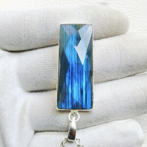 May include: A rectangular labradorite pendant featuring a faceted surface with deep blue and iridescent flashes. The gemstone is set in a silver-toned metal frame and attached to a delicate silver-toned chain, showcasing a vertical striped pattern.