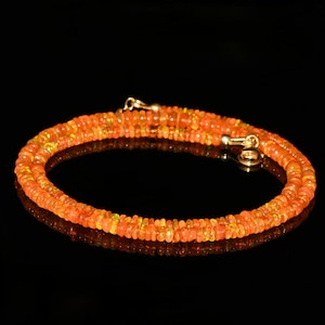 May include: A necklace composed of small, round, orange beads. The beads are strung together, forming a double strand. The necklace has a gold clasp and is displayed against a black background.