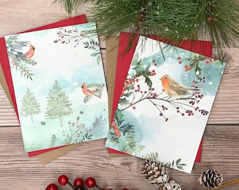 May include: Two Christmas cards with winter scenes. One card features a robin on a branch with red berries. The other card features two cardinals in a snowy forest. Both cards have a watercolor style.