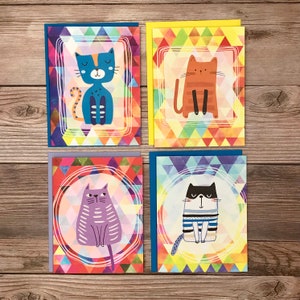 May include: Set of four greeting cards featuring colorful geometric patterns and illustrations of cats. Each card has a different cat design with a unique color scheme. The cards are perfect for sending a cheerful message to a friend or loved one.