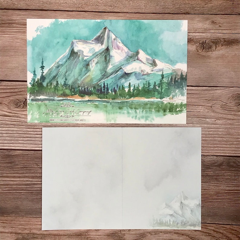 K&ouml;nnte beinhalten: Ein Aquarellbild einer Bergkette mit einem See im Vordergrund. Die Berge sind schneebedeckt und der See ist hellblau. Das Bild ist auf einer wei&szlig;en Karte mit dem Text "Little Wren Card Company" und einer Website-Adresse.