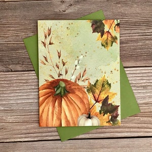 May include: A watercolor illustration of a pumpkin, fall leaves, and wheat stalks on a green background with gold speckles.