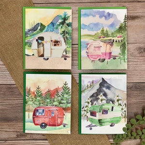 May include: Set of four watercolor greeting cards featuring vintage camper trailers in various scenic landscapes. Each card depicts a different color camper, including white, pink, red, and green, with a unique mountain or forest backdrop.