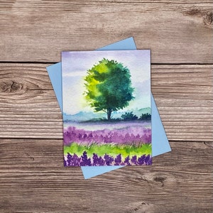 May include: Watercolor painting of a green tree in a field of purple flowers. The sky is a light blue with a hint of yellow.