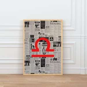 May include: A framed poster featuring a newspaper-style background with the red Libra zodiac symbol. The poster includes the words "DAILY NEWS" and "horoscopes". The frame is a light wood color.
