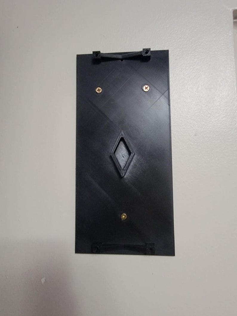May include: A black plastic wall mount with two small gold screws and a diamond-shaped opening in the center.