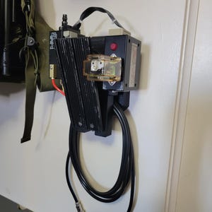 May include: A black air compressor with a red button and a clear plastic filter. The compressor is mounted on a wall with two black cords hanging down.