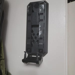 May include: A black wall mount with a textured surface and a small shelf. The mount has two screws on the bottom and a rectangular opening on the top.