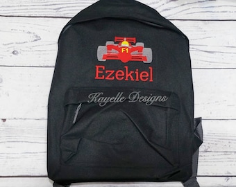 May include: Black backpack with a front pocket and a top flap. The backpack features an embroidered red race car design with the text "F1" and the name "Ezekiel" in red. The text "Kayelle Designs" is also embroidered on the front pocket.