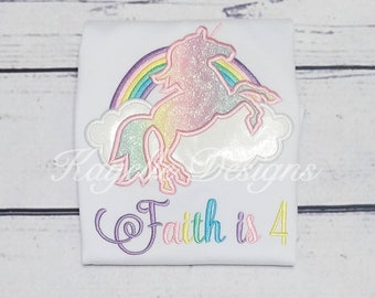 May include: White t-shirt with an embroidered unicorn jumping over a rainbow with clouds. The text "Faith is 4" is embroidered below the unicorn.