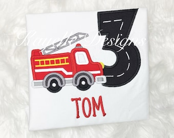 May include: Red fire truck with a black number three and the name Tom embroidered on a white t-shirt.