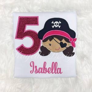 May include: White t-shirt with pink glitter number 5, a pink and black pirate girl design, and the name "Isabella" embroidered in pink.