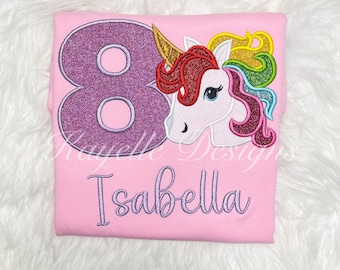 May include: Pink t-shirt with a purple glittery number 8 and a rainbow unicorn with a red mane. The shirt also has the name "Isabella" embroidered on it.