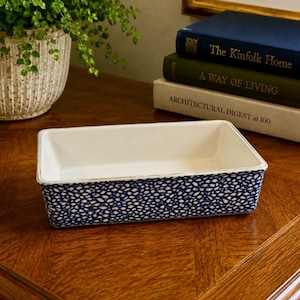 May include: A rectangular ceramic baking dish with a white interior and a blue and white speckled pattern on the exterior sides. The dish has a smooth, glossy finish and a clean, simple design, suitable for serving or preparing various food items.