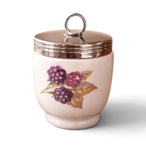 May include: A white ceramic jar with a rounded body and a pedestal base. The jar features a painted illustration of dark purple blackberries and green leaves on the front. It includes a polished silver-tone metal lid with a circular ring handle.
