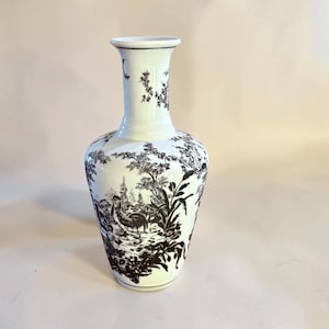 May include: A white ceramic vase with a narrow neck and a flared rim, featuring a detailed black transferware pattern of a rooster, foliage, and rural landscape elements that wrap around the entire body of the vessel in a continuous design.