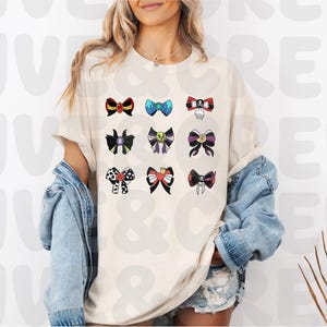 Op de afbeelding: Cr&egrave;mekleurig T-shirt met een verzameling kleurrijke strikdesigns. De strikken vari&euml;ren in stijl en kleur, waaronder zwart, rood, blauw en paars. Op het shirt staat de tekst "FIVE & CREW".