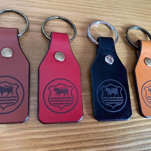 May include: Four leather keychains with silver key rings. Each keychain features a brown, red, black, or orange leather tag with a black and white silhouette of a bull inside a shield.