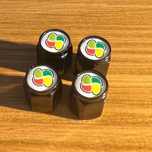 May include: Four black tire valve caps with a colorful sushi design. Each cap features a white circle with a green, red, and yellow four-leaf clover design.