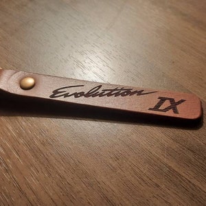 May include: A brown leather keychain with a metal ring. The keychain is engraved with the text "Evolution IX".
